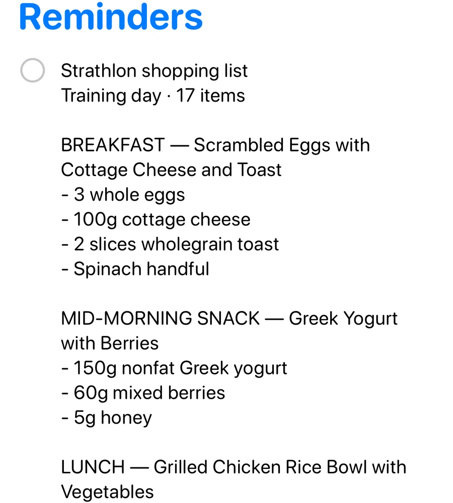 The Reminders app with one reminder, Strathlon shopping list, Training day, 17 items, then the list meal by meal: BREAKFAST, Scrambled Eggs with Cottage Cheese and Toast: 3 whole eggs, 100g cottage cheese, 2 slices wholegrain toast, spinach handful; MID-MORNING SNACK, Greek Yogurt with Berries: 150g nonfat Greek yogurt, 60g mixed berries, 5g honey; then LUNCH, Grilled Chicken Rice Bowl with Vegetables, running on past the bottom of the card.